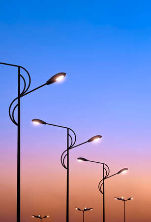 Silhouette row of modern street lampposts against colorful dramatic sky background in low angle view and vertical frameの写真素材