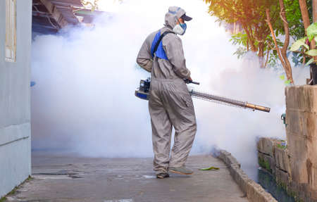 Outdoor healthcare worker using fogging machine spraying chemical to eliminate mosquitoes and prevent dengue fever on overgrown in slum areaの写真素材