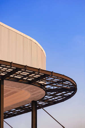 Curved metal awning structure with corrugated steel roof of modern building in construction site against blue sky in vertical frameの写真素材