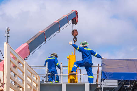 Rear view of 2 Asian engineer with crane truck are working to transferring yellow hydraulic cylinder...