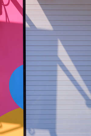 Sunlight and shadow on surface of stainless steel folding door with multi colored wall decoration in...
