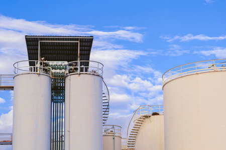 Storage fuel tanks with silos and pipeline system against clouds on blue sky in chemical and...