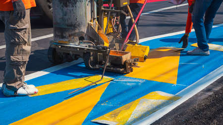 Low section of road workers group with thermoplastic spray road marking machine are working to paint...