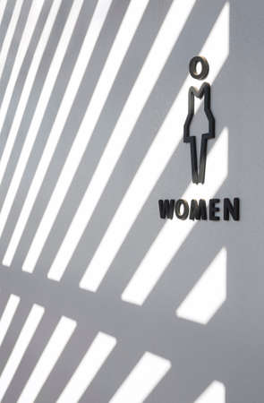 Abstract light and shadow pattern on surface of black wooden female restroom sign on white cement wall in perspective side viewの写真素材