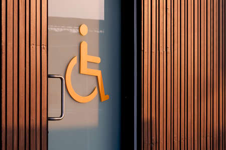 Perspective side view of disabled wheelchair restroom sign on glass sliding door with wooden wall in...