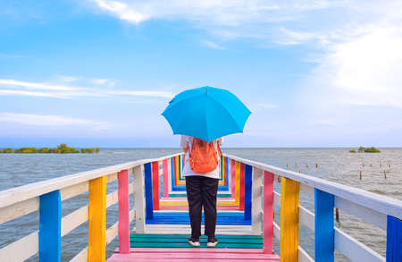Rear view of female tourist with backpack holding umbrella on the old multicolored wooden bridge at...