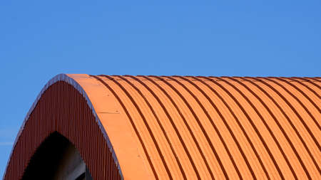 Orange curved corrugated steel roof against blue clear sky backgroundの写真素材