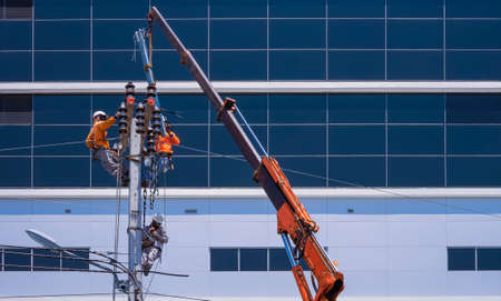 Asian electricians group with crane truck are installing electrical transmission on power poles in...