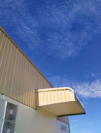 Low angle view of corrugated steel awning on warehouse building wall against clouds on blue sky...