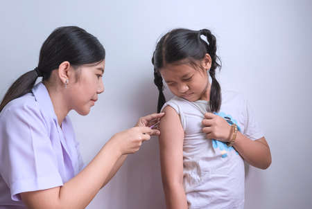 Asian female nurse giving vaccine to little girl at clinic during immunization campaign for childrenの写真素材