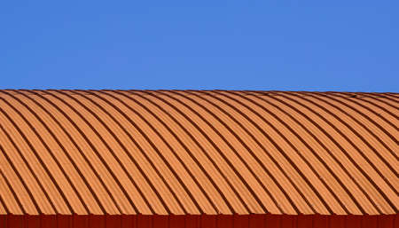 Curve line pattern of orange corrugated steel curved roof against blue clear sky background
