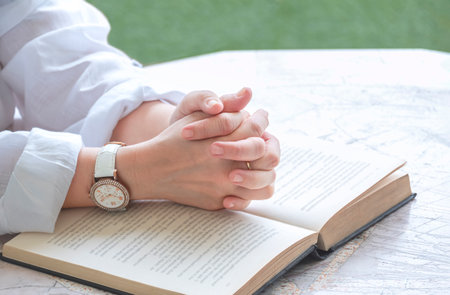 Close up of adult woman hands praying with open Holy Bible on octagon marble table in porch area at homeの写真素材