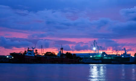 Beautiful dramatic twilight sky over nautical vessel at harbor in industrial area along the river after sunsetの写真素材