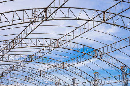 Curve lines pattern of metal roof beam structure of large dome event tent against clouds on blue sky...
