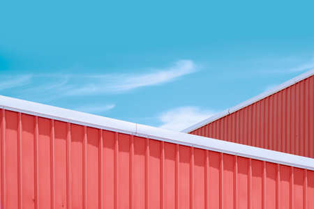 Minimal exterior architecture background of orange corrugated steel rooftop of industrial buildings against blue sky in pastel color tone styleの写真素材