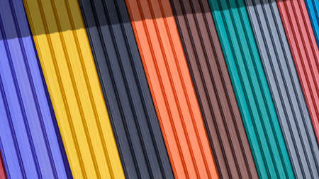 Diagonal pattern of multi colored corrugated metal sheets for roofing on display stand with sunlight and shadow on surfaceの写真素材