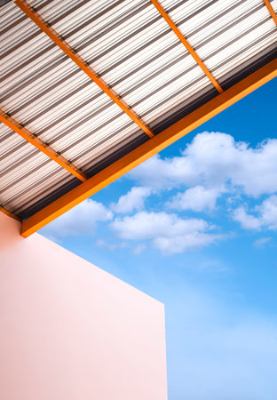 Low angle view of arcade roof with beige warehouse building against clouds on blue sky in vertical frameの写真素材