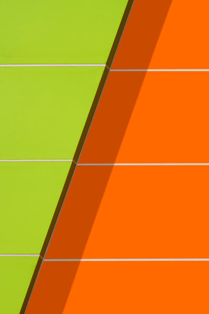 Sunlight and shadow on surface of vibrant green and orange aluminum composite tiles exterior wall decoration of modern building in vertical frameの写真素材