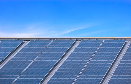 Many solar panels on steel roof of industrial building against blue sky background