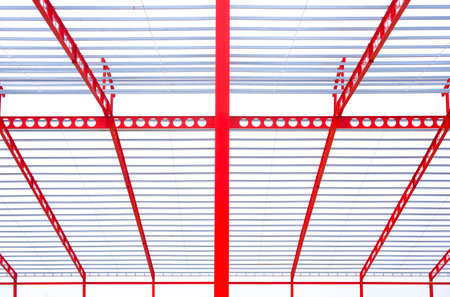 Red metal castellated beam with steel roof structure of industrial building in construction site against white cloudy sky backgroundの写真素材