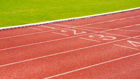 Red synthetic running tracks with numbers and green field in athletic outdoors stadium