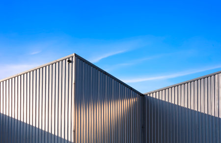 Corrugated Steel Wall of industrial Warehouse Building against blue sky background with sunlight and shadow on surfaceの写真素材