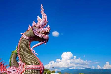 Side view of colorful traditional serpent statues on bannister of Thai temple against cloud on blue...