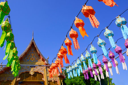 Decorative colorful hanging paper Lanna lanterns in front of the old Thai temple against blue sky backgroundの写真素材