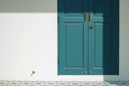 Light and shadow on surface of vintage green wooden door with brass door handle on white cement wall...