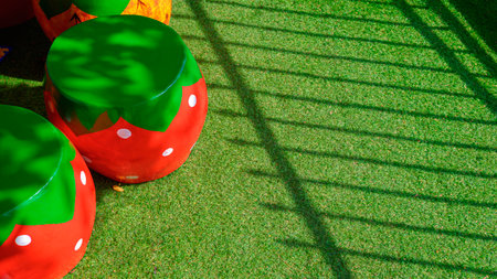 Sunlight and shadow on surface of decorative stucco garden seats in strawberry shape on artificial turf in front yard areaの写真素材