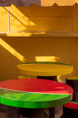 Focus at decorative stucco garden table in watermelon shape in front of colorful yellow coffee street kiosk in vertical frameの写真素材