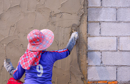 Rear view of female Construction Laborer plastering cement on concrete block wallの写真素材
