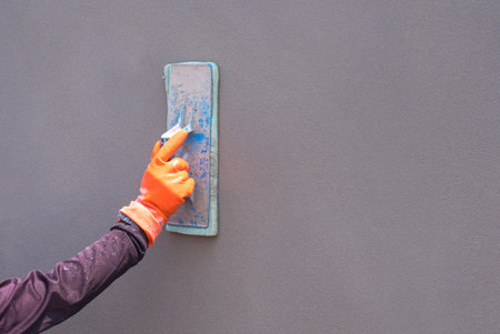 Close up of construction worker Hand in Rubber Glove Polishing Cement Wall in construction site, perspective side view with copy spaceの写真素材