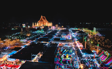 Aerial view of beautiful decorative lighting on Thai temple and lots of booths, amusement park, thrilling plaything with crowd of people in annual festival area at night in Samut Sakhon, Thailandのeditorial素材