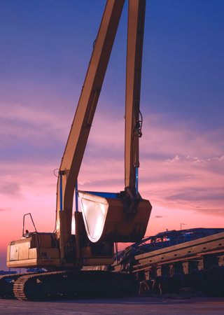 Excavator and barge waiting to be unloaded at harbor against twilight sky after sundown in vertical frameの写真素材