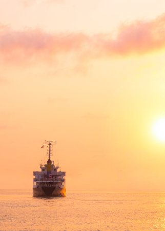 Silhouette Oil Tanker Ship is sailing in the sea with beautiful golden sunlight at sunset time in vertical frameの写真素材