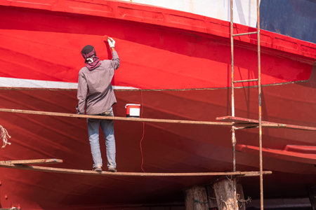 Asian painter on hanging platform is repainting hull of the old wooden fishing boat in shipyard area, improvement and renovation conceptの写真素材