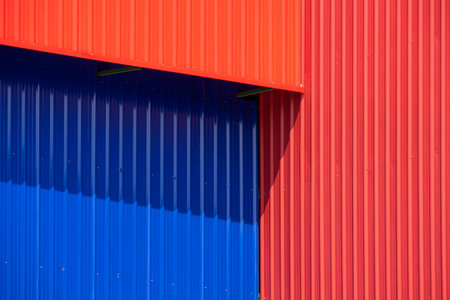 Background of red and blue corrugated metal wall with roof awning of warehouse building with sunlight and shadow on surface, Perspective side viewの写真素材