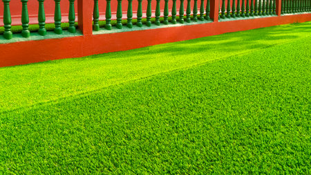Background of green artificial turf with balusters of red vintage fence, side view with copy spaceの写真素材