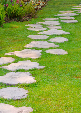 The old wooden plank-shaped garden path made of artificial stone material on green lawn with ornamental bush in public park area and vertical frameの写真素材