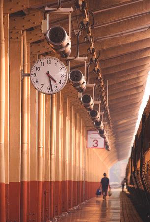 Focus at vintage hanging wall clock and loudspeaker with blurred background of passengers walking on...