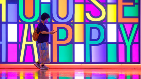 Asian female passenger using smartphone while walking through colorful illuminated lighting wall in subway building area at Bangkok, Thailandの写真素材