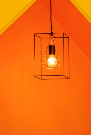 Illuminated modern metal cage hanging lamp in front of colorful street coffee kiosk in vertical frameの写真素材