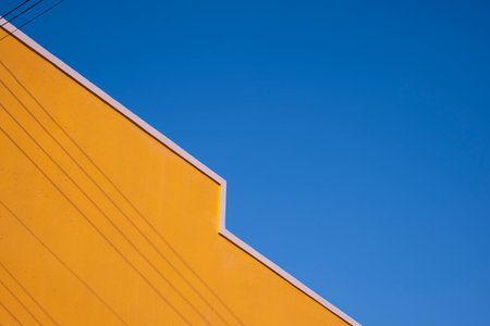 Street Minimal Architecture style of colorful yellow Building Wall with shadow of electric cable lines on surface against blue clear sky Backgroundの写真素材