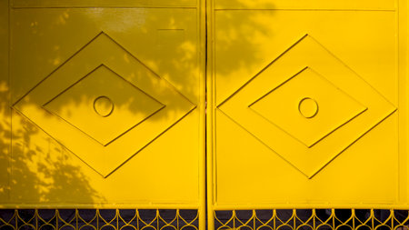 Sunlight and branch shadow on geometric pattern surface of yellow metal gate door with wrought iron in front of homeの写真素材