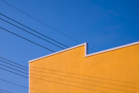 Street Minimal Architecture style of the old Vintage yellow Building Wall with electric cable lines against blue clear sky Background, Perspective low angle viewの写真素材