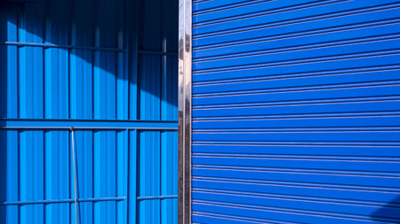 Focus at blue roller shutter door with blurred background of corrugated steel interior wall of modern warehouse in perspective side viewの写真素材