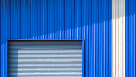 Automatic roller shutter door and white stripe on blue corrugated metal wall of warehouse buildingの写真素材