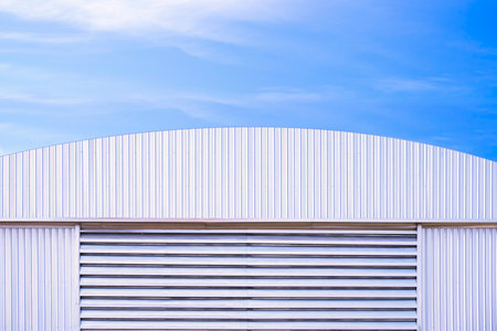 Aluminium louver on corrugated steel wall of warehouse building with curve metal roof against blue sky backgroundの写真素材