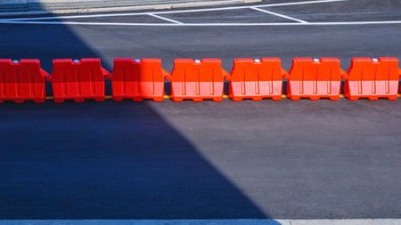 Row of orange plastic barriers on the middle of asphalt road in outdoor car parking with sunlight and shadow on surfaceの写真素材